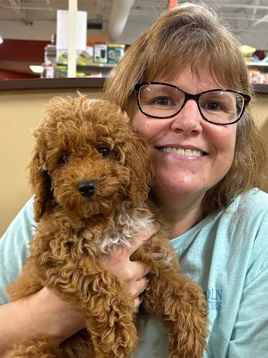 Woman with glasses holding a curly brown puppy